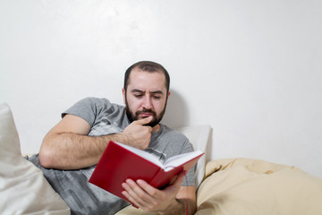 Young man pensive reads a book in the bedroom. White background.