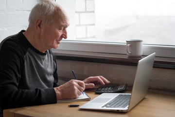 An old man who counts on a calculator and enters information into a computer.