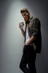 Wall Mural - Shot of handsome young bearded man in a plaid shirt having coffee Male taking rest and drinking fresh morning coffee Young hipster bearded man in shirt with coffee in hand.