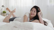 © PRPicturesProduction - Beautiful asian woman with lovely smile lying on her stomach relaxing. young girl resting on bed looking aside in cozy bedroom at home. pretty korean female smiling enjoy leisure time in modern room.