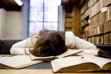 Tired girl in the reading room of the library to prepare for the exam falling asleep on an open book