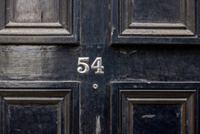 House Number 54 With The Fifty-four In Silver Numbers Screwed To A Black Wooden House Door