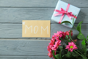 Greeting card with flowers and gift for Mother's Day on wooden table