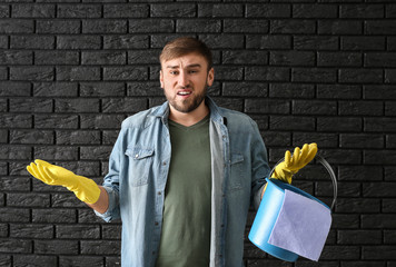 Poster - Disappointment lazy man with cleaning supplies on dark brick background