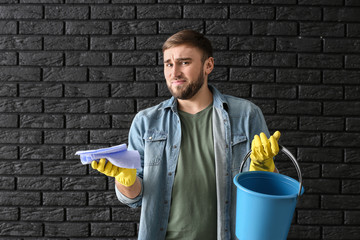 Poster - Disappointment lazy man with cleaning supplies on dark brick background