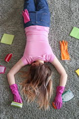 Tired housewife with cleaning supplies lying on soft carpet