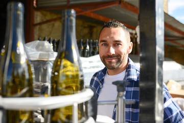 Wall Mural - young man wine maker working filling wine bottle with automatic bottling machine