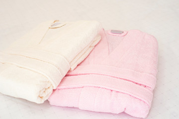 Folded bathrobe on bed in room. White and pink, two robes