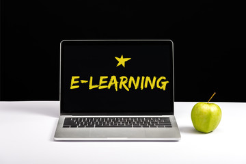 fresh green apple and laptop on table with e-learning lettering and star on screen isolated on black