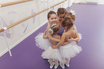 Wall Mural - Top view shot of a group of cute little ballrinas wearing violet leotards and tutus hugging together after ballet class. Happy little girls embracing together at ballet school, copy space