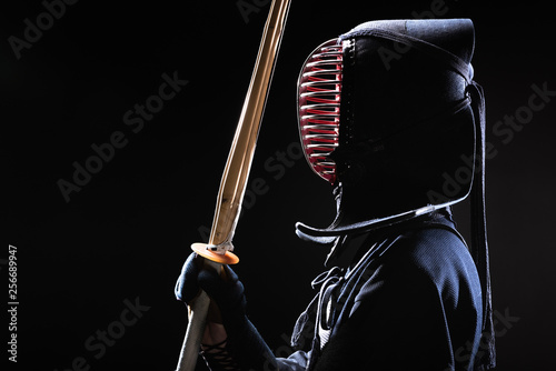 Plakaty Kendo  widok-z-boku-wojownika-kendo-w-tradycyjnym-helmie-trzymajacym-bambusowy-miecz-na-czarno