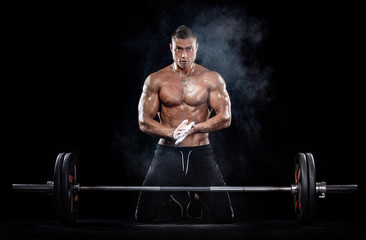 Photo of strong muscular bodybuilder athletic man pumping up muscles with barbell on black background. Workout energy bodybuilding concept.