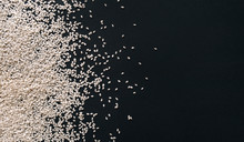Scattered white sesame seeds on black textured paper background. Calcium concept. Close up, copy space, top view.