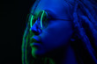 © Alex - beautiful girl in the light of neon colored lamps light blue green on black background wearing glasses
