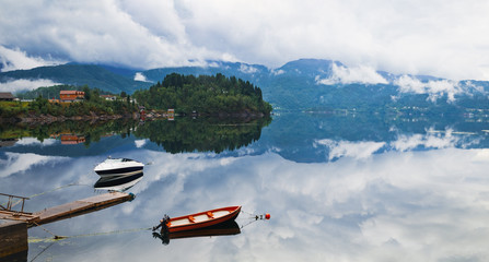 View from Samnanger on waters of Samnangerfjorden in Hordaland county, Norway. Two lonely boats on calm water of fjord, summer shore with magnificent reflections