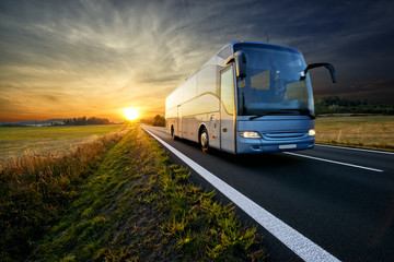 bus traveling on the asphalt road in rural landscape at sunset