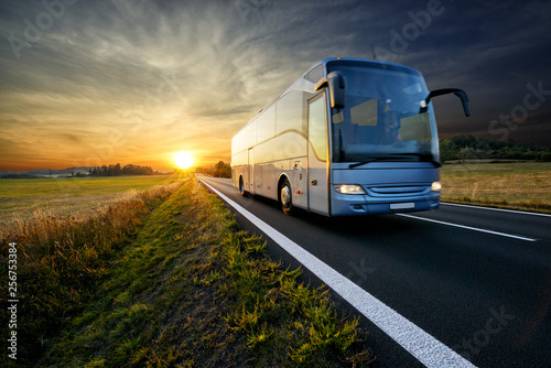 Fotomural Bus traveling on the asphalt road in rural landscape at sunset