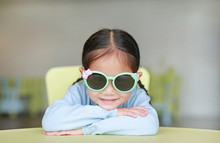 Adorable Little Asian Child Girl Laying On Children Table Wearing Sun Glasses With Smiling And Looking At Camera, Happy Kids.
