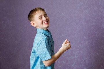 A male child in a blue shirt against a purple wall shows with a finger that everything is cool. He dabbles and laughs.