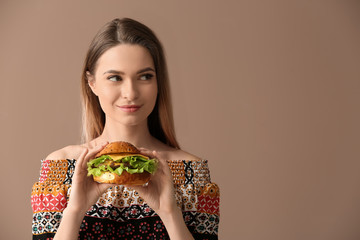 Beautiful young woman with tasty burger on color background