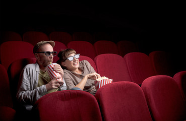 Wall Mural - Young cute couple sitting alone at red movie theatre and having fun