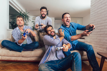 Smiling male friends playing video games at home and having fun.