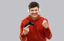 Technology, Gaming And People Concept - Young Man Or Gamer In Headphones With Gamepad Playing Video Game