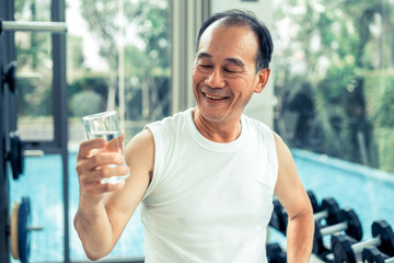 Wall Mural - Senior man drink mineral water in gym fitness center after exercise. Elderly healthy lifestyle.