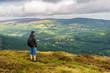 Tourist enjoying the beautiful view and resting on the top of Maulin Peak, Wicklow Mountains, after a hike on a cloudy summer day. 40 shades of green of Ireland.