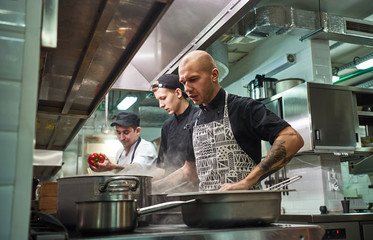 Wall Mural - Concentrated at work. Professional team of chef and two young assistants cooking in a restaurant kitchen