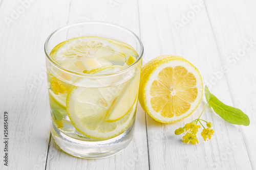 Photographie Refreshing drink for health, lemon water in a glass and yellow linden flowers on a white table