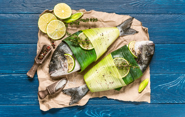 two fresh raw dorado fish, wrapped in palm leaves, sprinkled with a mixture of peppers and large gimolais salt, with slices of lime and lemon, ready to be baked. cooking dinner concept for two