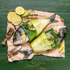 two fresh raw dorado fish, wrapped in palm leaves, sprinkled with a mixture of peppers and large gimolais salt, with slices of lime and lemon, ready to be baked. cooking dinner concept for two