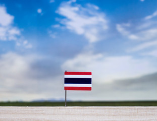 Flag of Thailand with vast meadow and blue sky behind it.