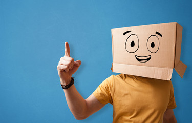 Young man standing and gesturing with a cardboard box on his head with drawn smiley face
