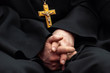 Golden cross with crucifixion of Jesus on the chest of a priest in black clothes. The symbol of the Orthodox religion. Hands together are blurred out of focus. Shallow depth of field.