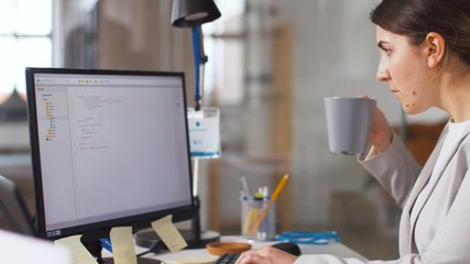 business, programming and technology concept - female programmer with script on computer screen working and drinking coffee at office