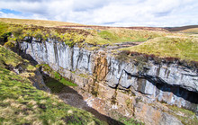 A Large Rock Chasm With Massive Cliffs In A Barren Grassy Landscape Near The Peak Of Pen-y-Ghent In The Peak District, England.