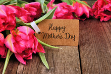 Happy Mothers Day Tag Close Up Among A Bouquet Of Pink Tulip Flowers Over A Dark Wood Background