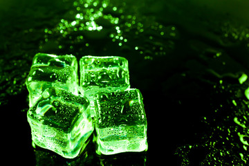 Green ice cubes on black wet table.