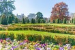 Colourful flowers fill the foreground during early spring in the Parterre Gardens (Spanish: Jardín del Parterre) of Madrid, Spain with large trees and buildings in the background. 