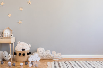 Stylish scandinavian newborn baby room with toys, children's chair, natural basket with teddy bear and small shelf. Modern interior with grey background walls, wooden parquet and stars pattern.