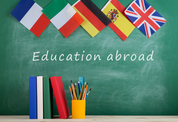 Fototapete - backpack, flags of Spain, France, Great Britain and other countries, books and school supplies of the blackboard