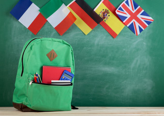 Fototapete - backpack, flags of Spain, France, Great Britain and other countries and school supplies on the background of the blackboard