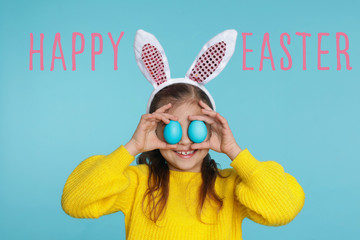 Sticker - Little girl in bunny ears headband holding Easter eggs near eyes on color background