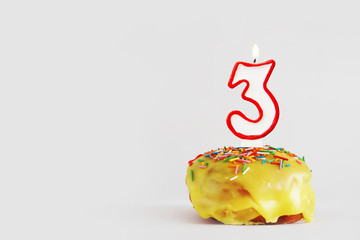 Three  years anniversary. Birthday cupcake with white burning candle with red border in the form of number Three. Light gray background with copy space