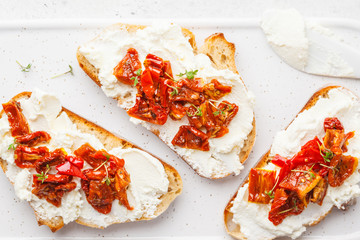 Ricotta and sun dried tomatoes sandwiches on white board.