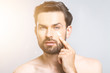 © denis_vermenko - Skin care. Handsome young shirtless man applying cream at his face and looking at himself with smile while standing over gray background and looking at camera. Close-Up. Space for text.