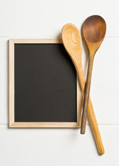 Wall Mural - Blank, empty, black chalkboard with wooden cooking spoons flat lay from above on white wooden table