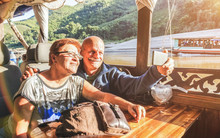Senior Retired Couple Of Happy Vacationers Taking Selfie At Mekong Exploration Tour With Slowboat In Laos PDR - Active Elderly Travel Concept On Trip Around The World - Warm Saturated Sunset Filter